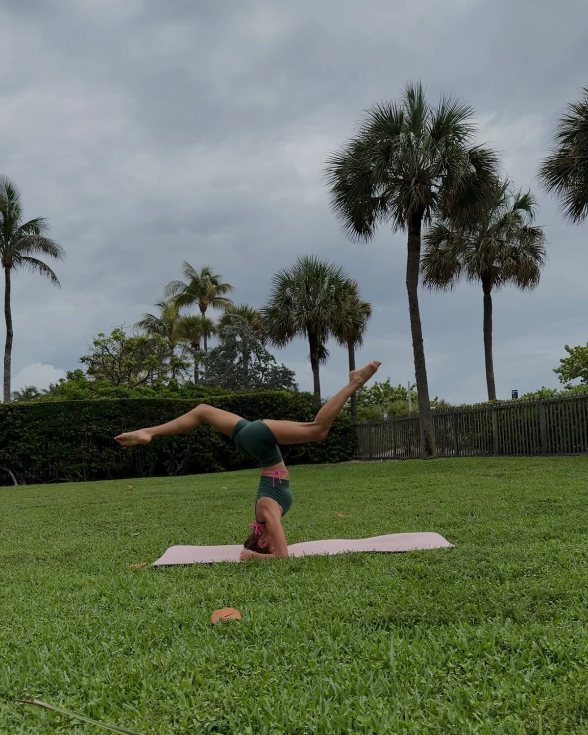 Julia practicing a headstand on a yoga mat beneath palm trees